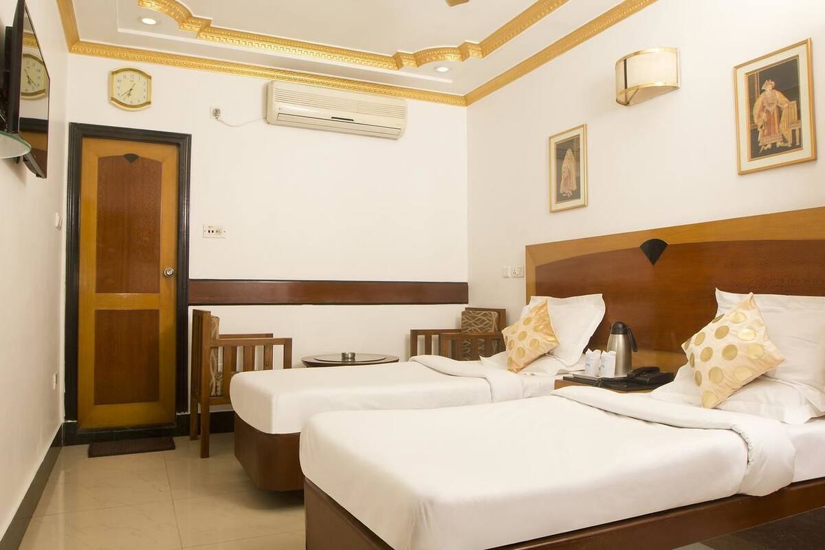Hotelkamer met twee bedden, een houten hoofdbord, een kleine tafel, een stoel, een klok en een wandairconditioner.