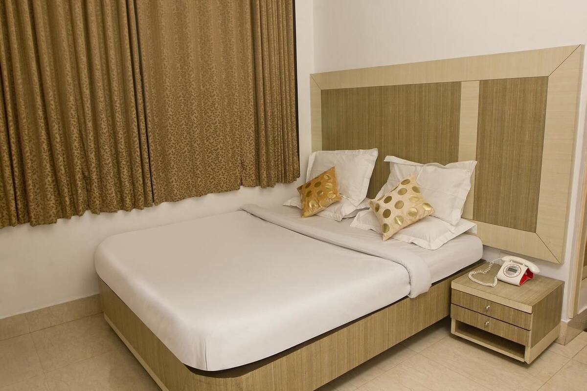 Een netjes opgemaakt bed met witte lakens, een houten hoofdbord en twee decoratieve kussens.