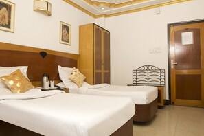 A hotel room with two beds, a wardrobe, a bedside table with a lamp, and a door with a sign. - Hotel White House (Kolkata)