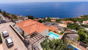 Uma área residencial com piscina, telhados de telha vermelha e vista para o mar.
