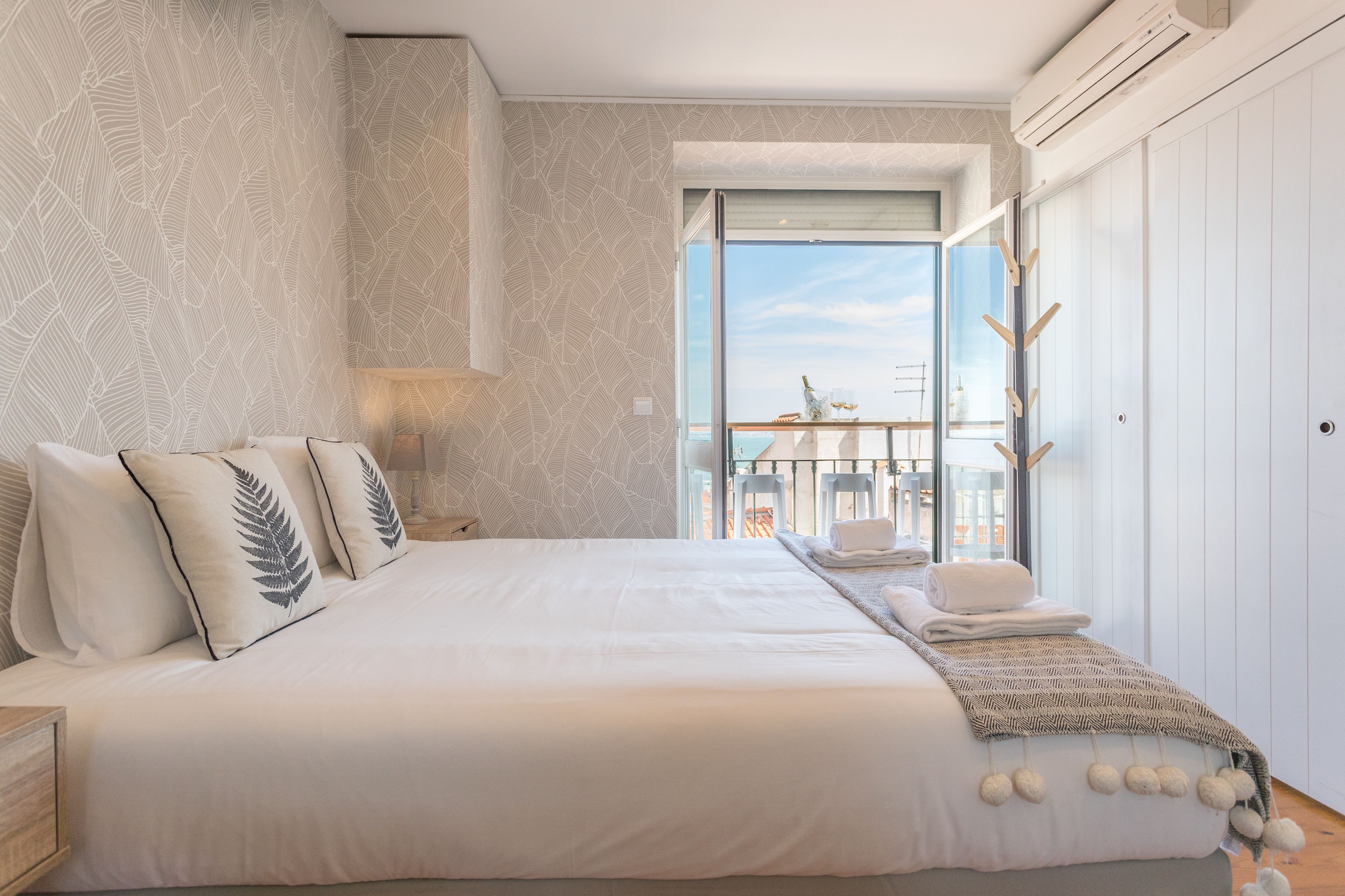 A bedroom with a large bed, a balcony with a view, and a wardrobe.