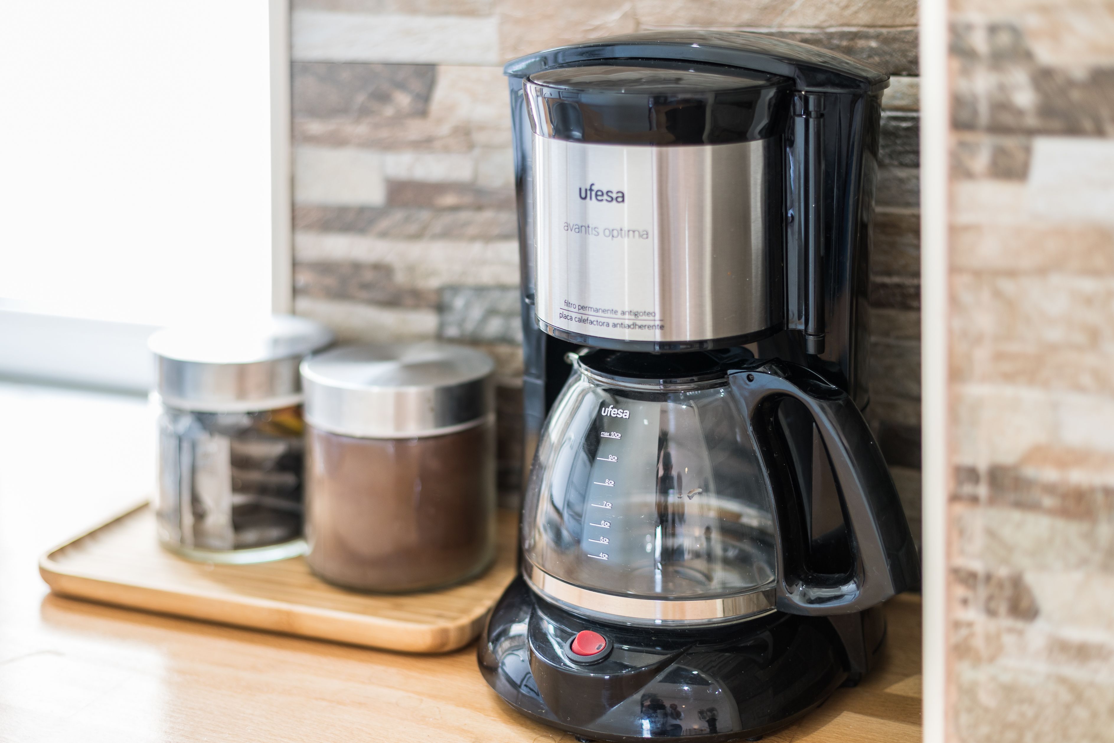 A black coffee maker with a transparent water reservoir and a stainless steel label.