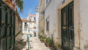 A narrow cobblestone street with buildings on either side, a green door, and potted plants. - Alfama Vintage Studio Apartment w/ RiverView - by LU Holidays (Lisbon)