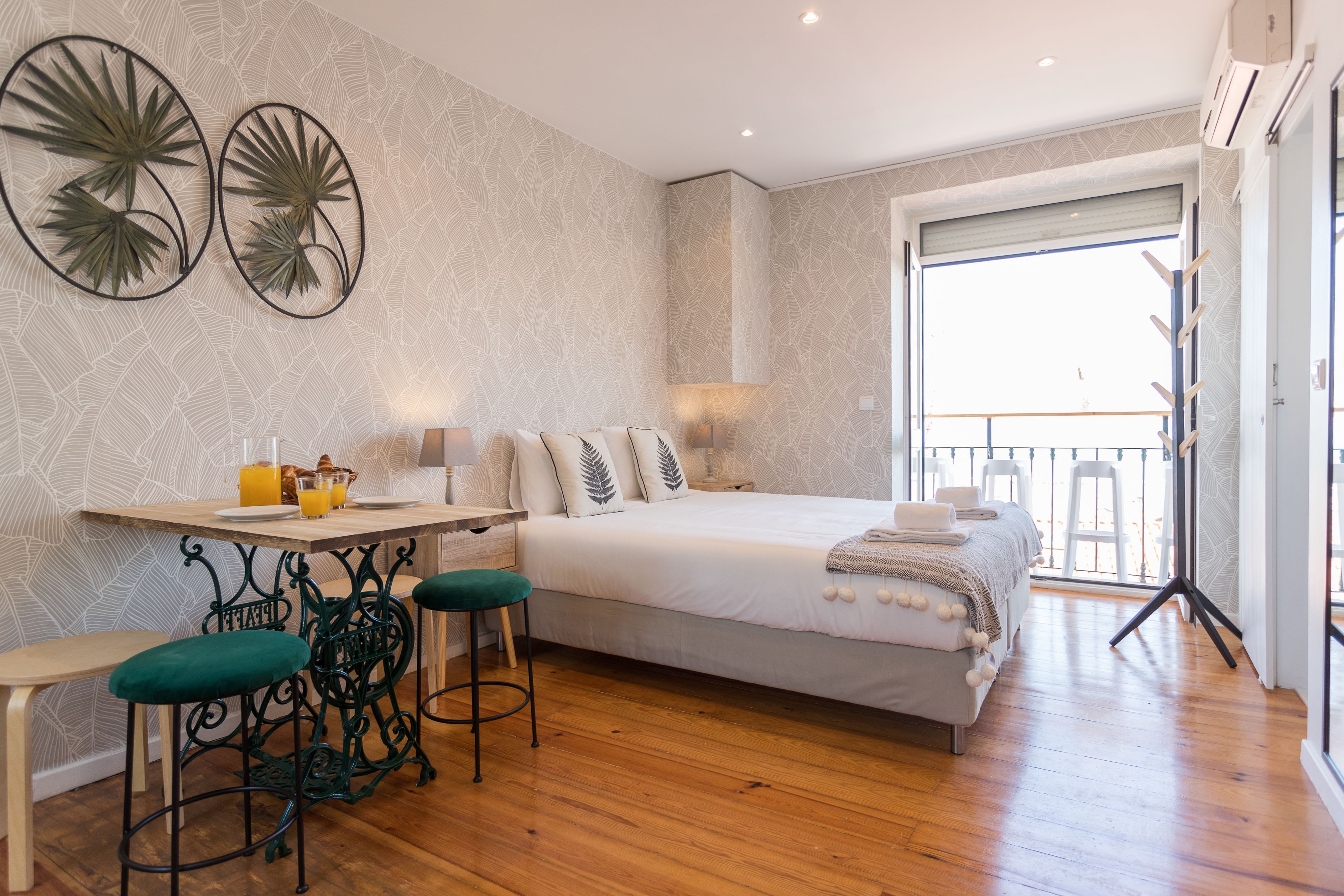 A bedroom with a bed, a desk, two chairs, a balcony, and a window.