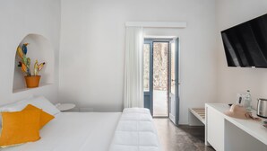 A modern hotel room with a bed, a desk, a potted plant, and a view of the outdoors.