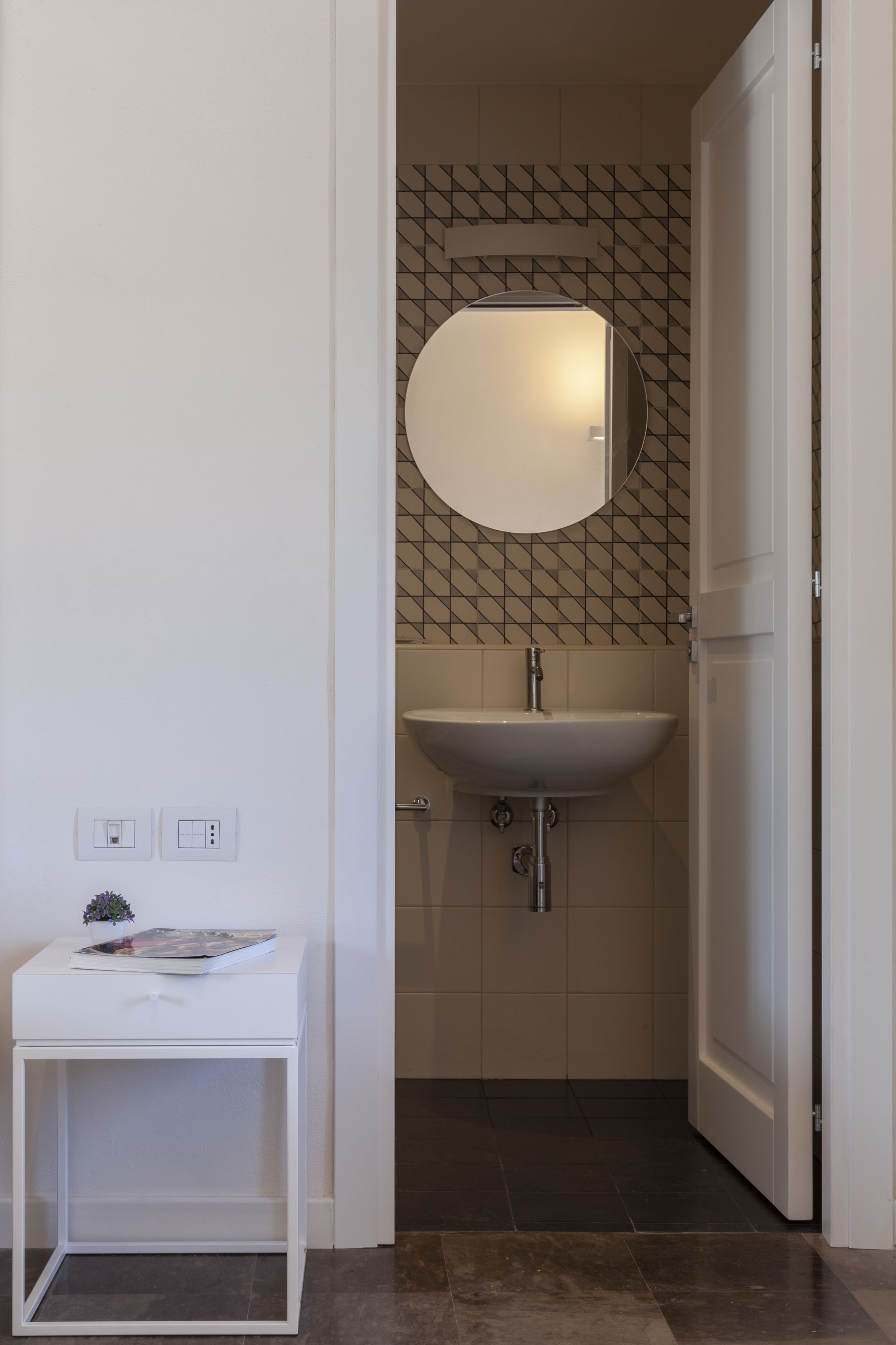 Un bagno con un lavandino bianco, uno specchio e un piccolo tavolo con una rivista.