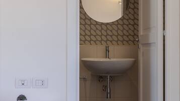 Un bagno con un lavandino bianco, uno specchio e un piccolo tavolo con una rivista.