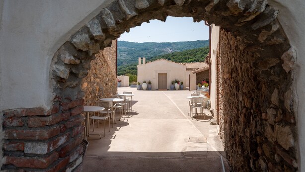 An outdoor patio area with tables and chairs, a stone archway, and a view of a hillside.