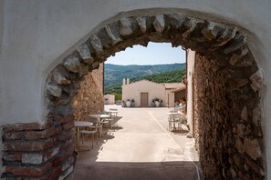 Un área de patio al aire libre con mesas y sillas, un arco de piedra y vistas a una colina.