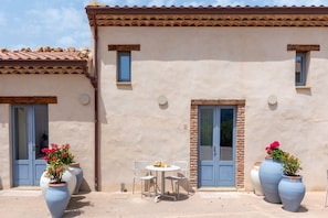 Un bâtiment avec un toit recouvert de tuiles, deux portes et un petit patio comprenant une table et des chaises.