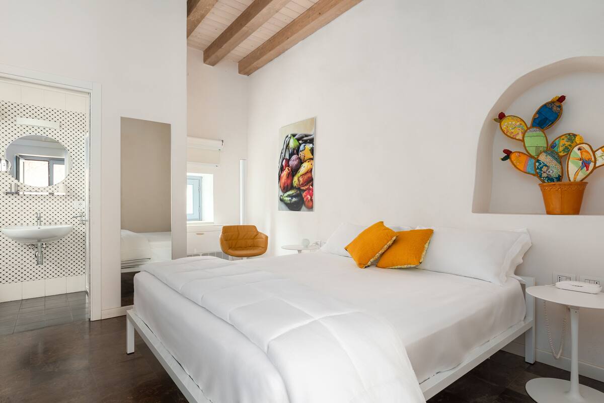 Een moderne slaapkamer met een groot bed, een witte wastafel, een spiegel en een wand met kleurrijke kunstwerken.