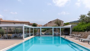 A rectangular swimming pool with clear blue water, surrounded by a glass enclosure and outdoor seating.
