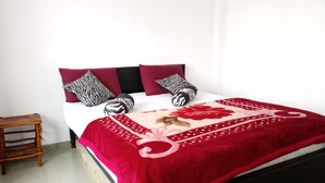 A bed with a red and beige bedspread, black and white patterned pillows, and a wooden nightstand to the left.