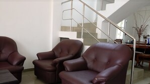 A modern living room with three leather armchairs, a dining table, and a staircase with metal railings.