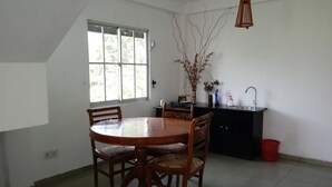 A dining area with a round table and four chairs, a window with blinds, a black cabinet with a sink, and a hanging light fixture.