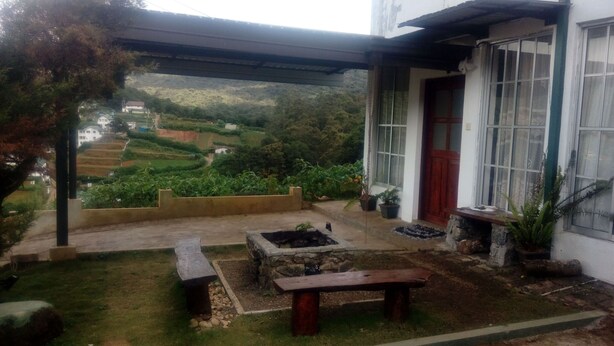 A covered outdoor area with a stone bench, a fire pit, and a view of terraced fields and houses in the distance.