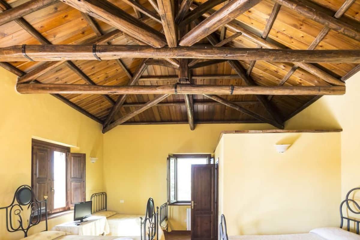 A rustic room with a wooden ceiling, two beds, a desk, and a window.