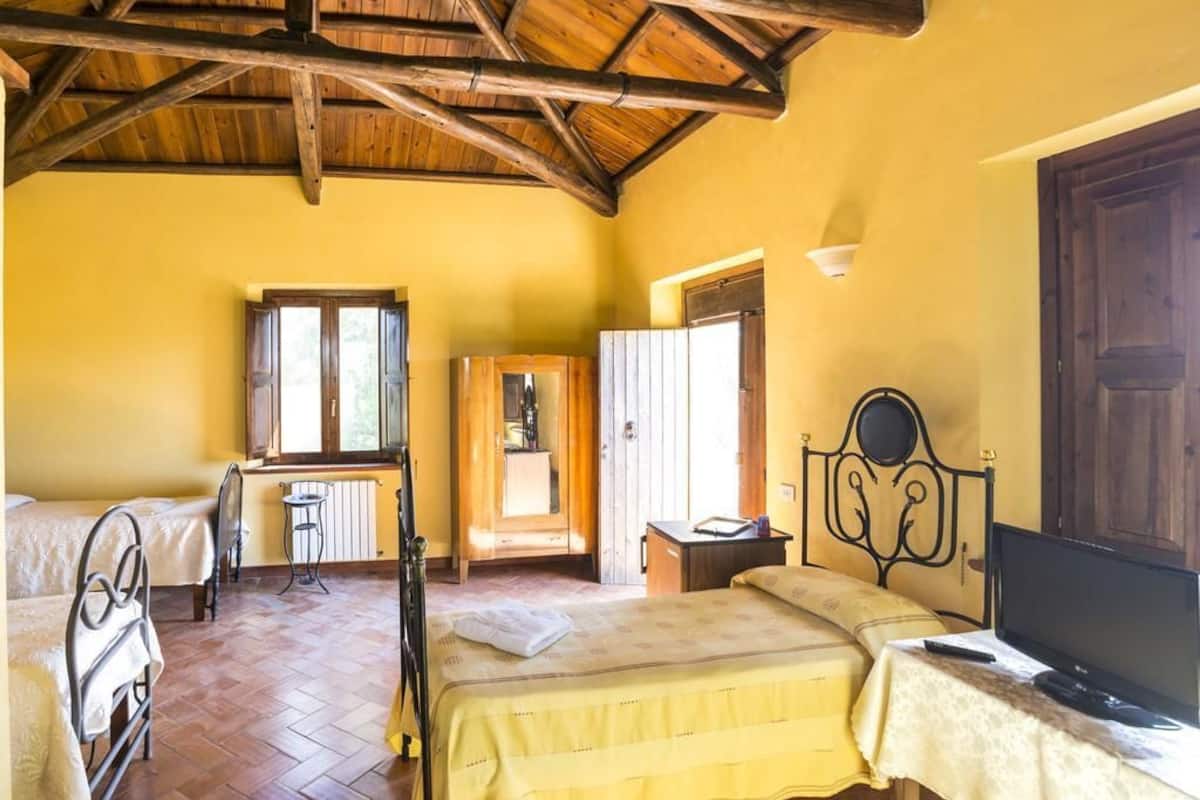 A room with two beds, a wooden ceiling, a window, and a television.