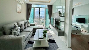 Un salon moderne avec un canapé, une table basse et un téléviseur. Une grande fenêtre offre une vue sur la ville.