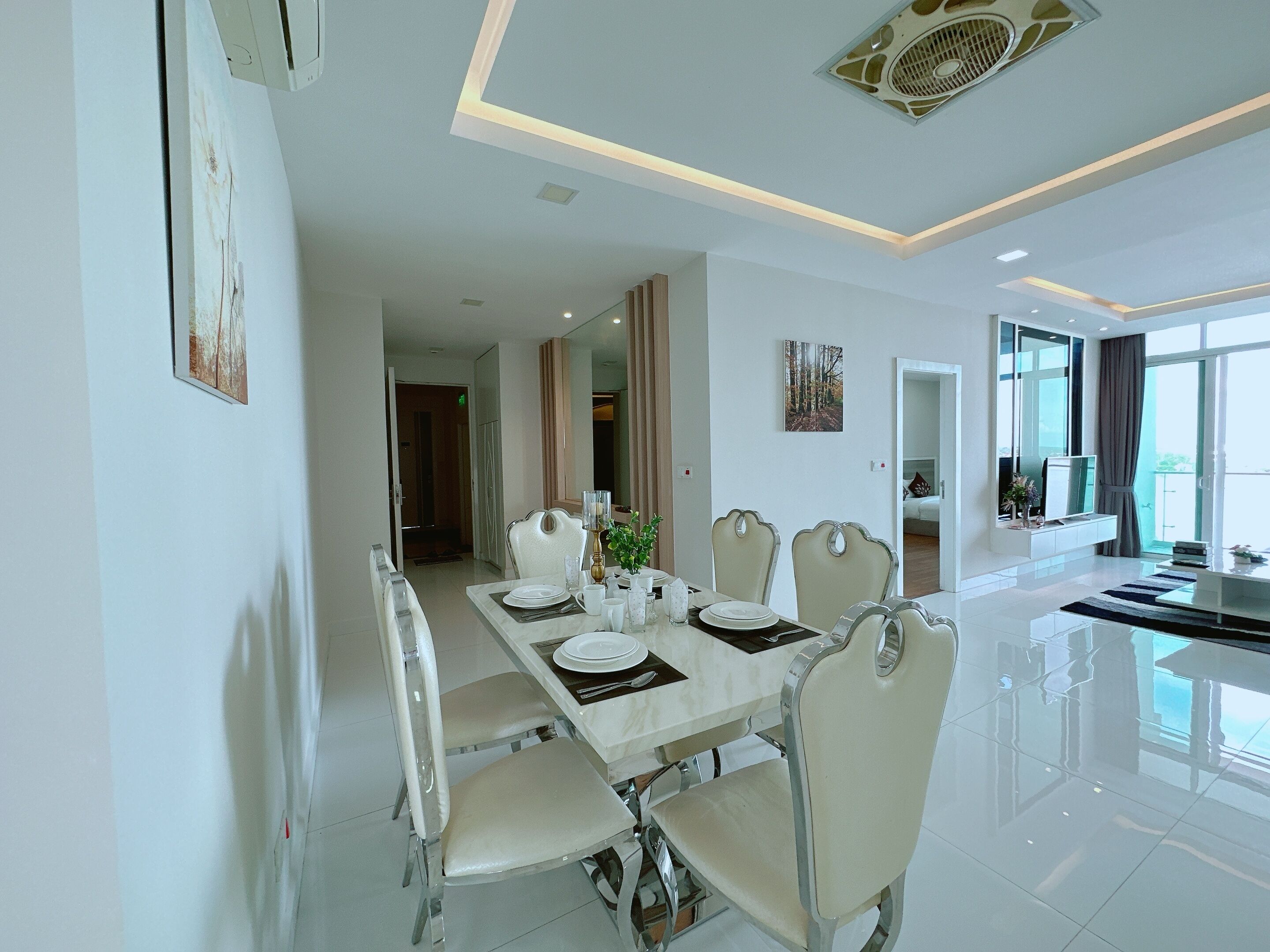 A modern dining area with a long table set for four, white chairs, and a contemporary ceiling design.