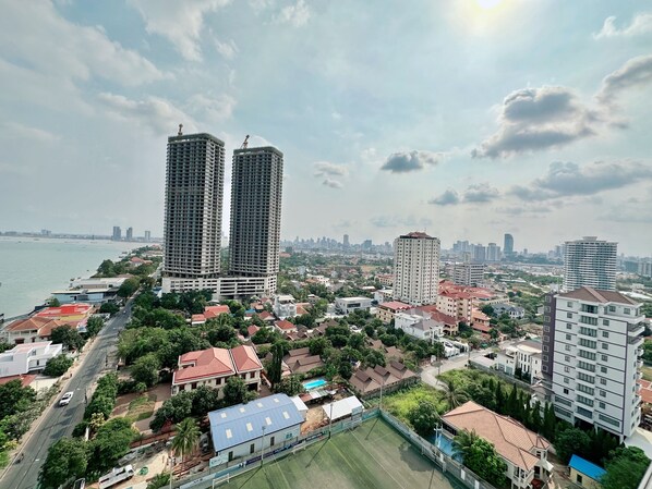A high-rise building with a construction crane, surrounded by smaller residential buildings and a body of water.