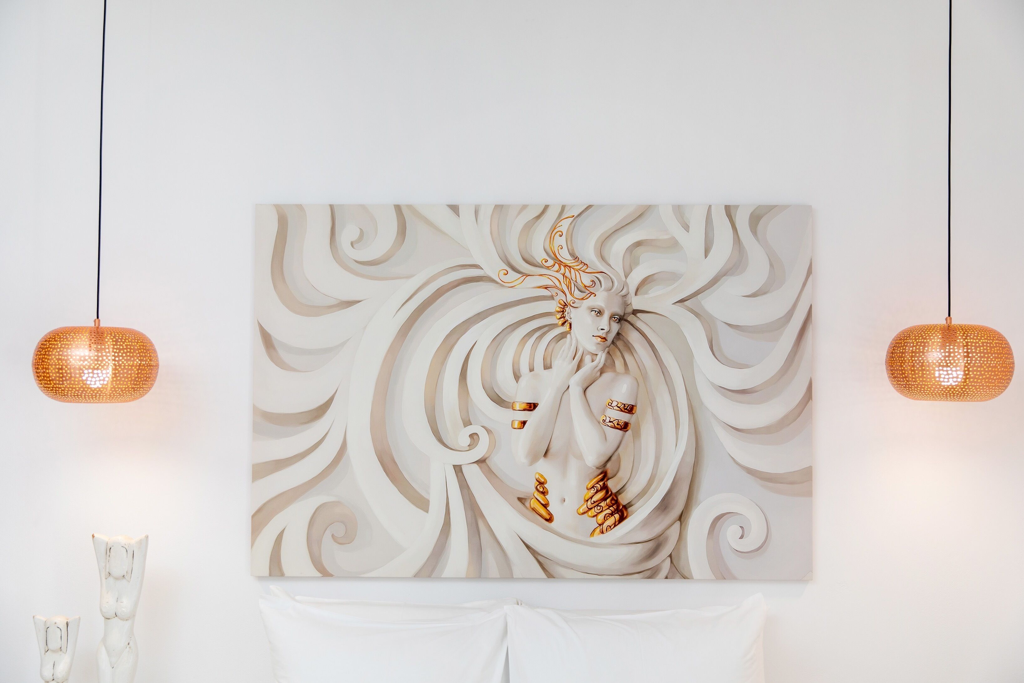A wall-mounted artwork with a central figure, two hanging pendant lights, and a white table with a white cloth.