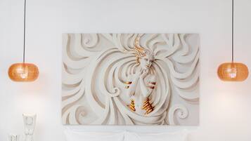 Una obra de arte mural con una figura central, dos lámparas colgantes y una mesa blanca cubierta con un paño blanco.