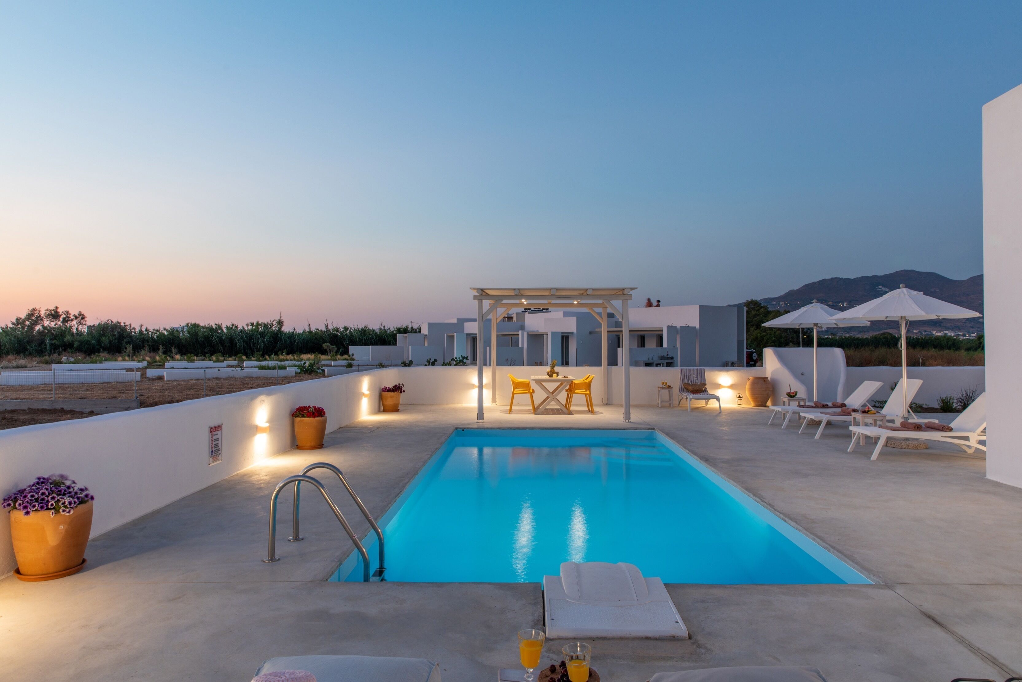 A rooftop pool area with a clear view of the mountains, a pergola, lounge chairs, and a table with chairs.