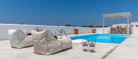Un espace piscine aménagé sur le toit, avec des chaises longues, une pergola et une table entourée de chaises.