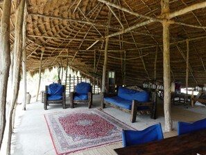 A rustic hut with a thatched roof, wooden furniture, and a patterned rug. - Wami River Bush Retreat - Kisampa (Saadani)