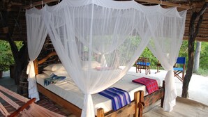 A wooden bed with a canopy, surrounded by chairs and a hammock.