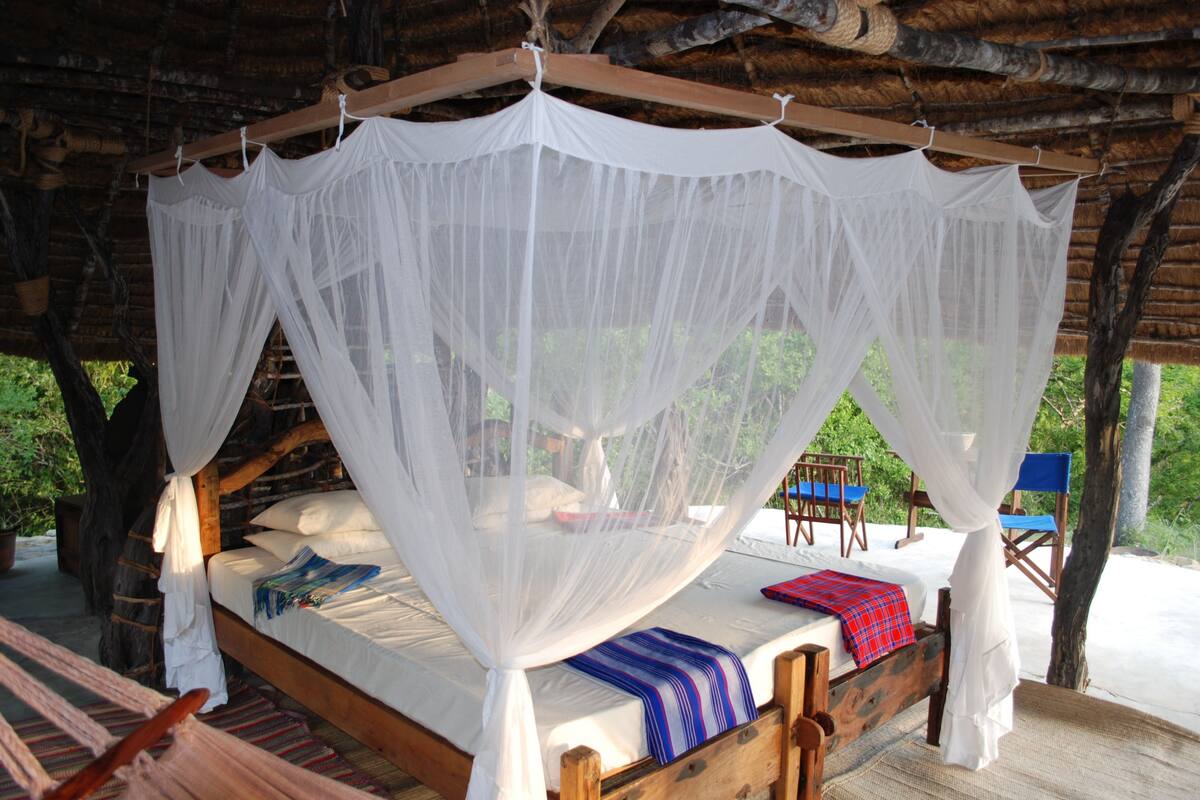 A wooden bed with a canopy, surrounded by chairs and a hammock.