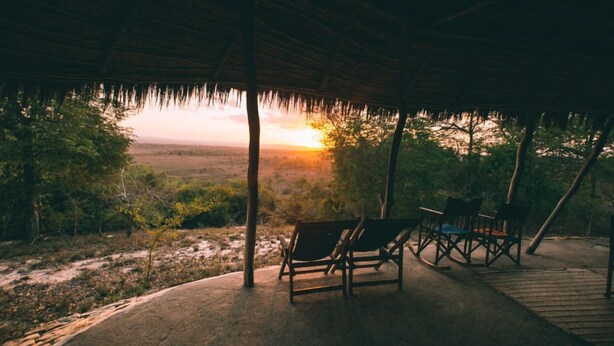 A covered outdoor seating area with chairs and a view of the sunset over a natural landscape.