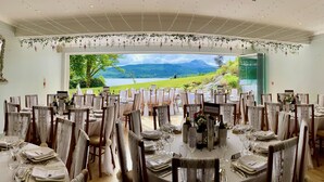 A dining area with tables set for a meal, a view of a lake and mountains, and a sign reading "ARROWTOWN". - Altskeith Country House on Loch Ard (Stirling)