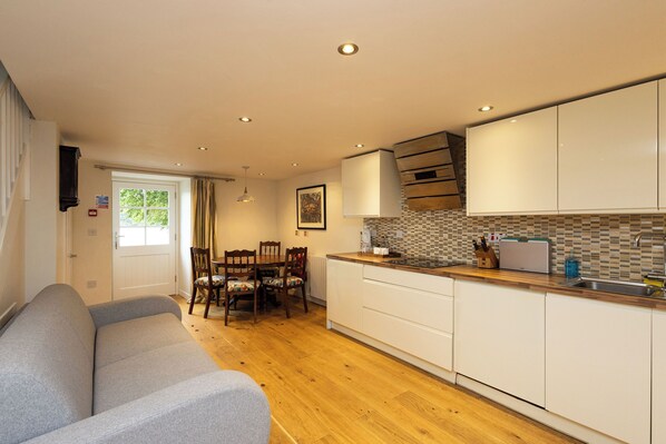 A modern kitchen with white cabinets, a wooden countertop, and a dining area with a sofa and chairs.