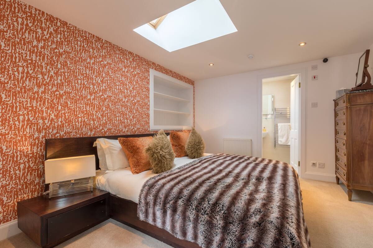 A bedroom with a skylight, a bed with a patterned blanket, a nightstand, and a wooden dresser.