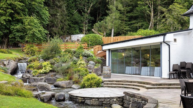 A modern house with a stone patio, a small waterfall, and outdoor furniture. - Altskeith Country House on Loch Ard (Stirling)