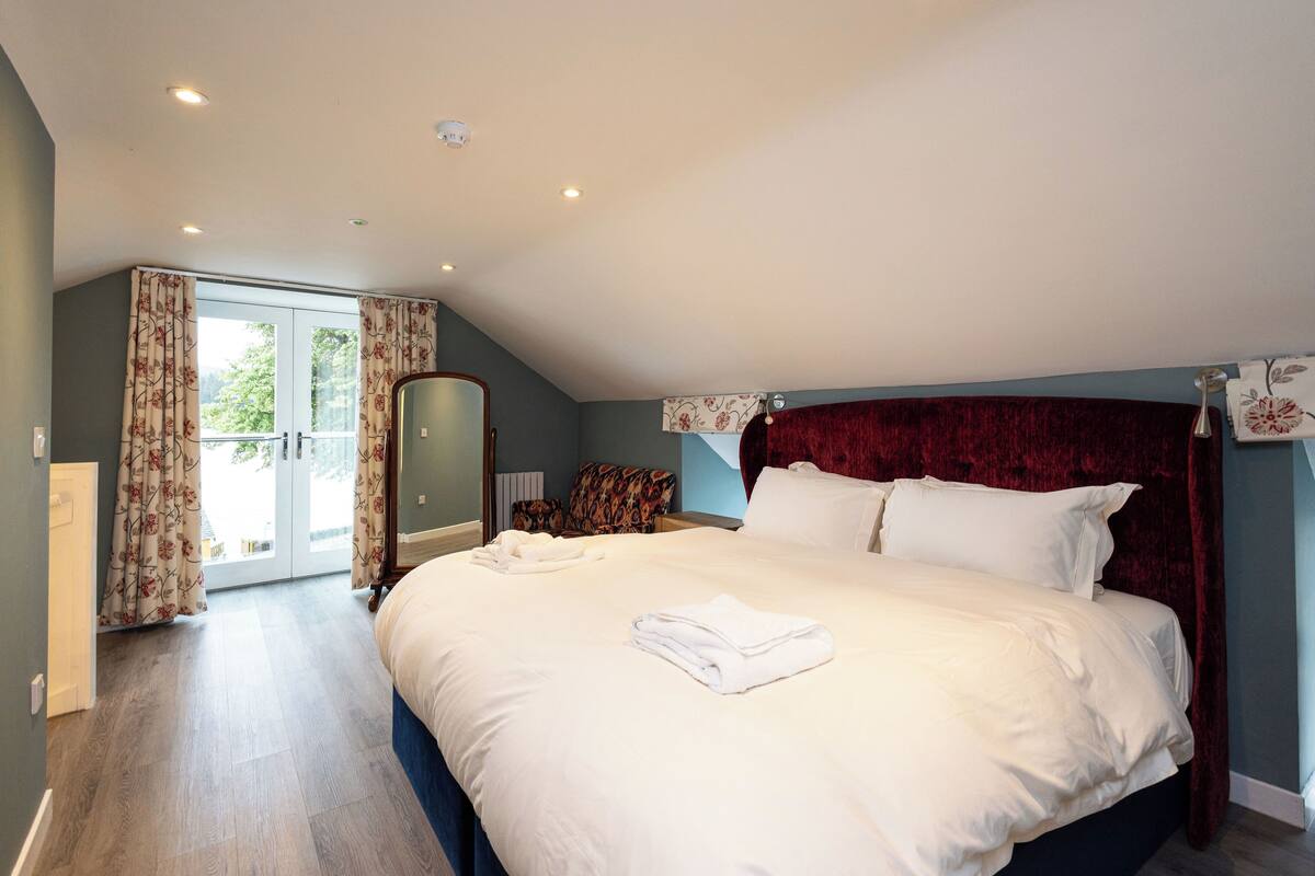 A bedroom with a large bed, a red headboard, and a view of the outdoors through a sliding glass door.