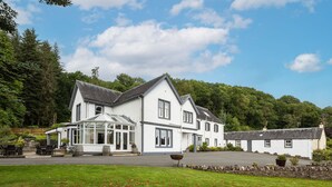 A large white building with a glass conservatory, surrounded by a well-maintained lawn and stone wall. - Altskeith Country House on Loch Ard (Stirling)
