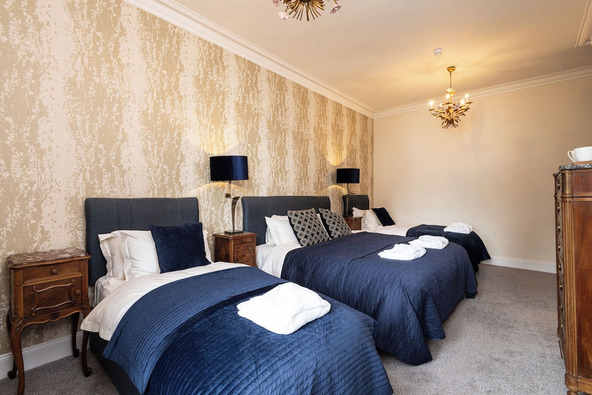 A hotel room with two beds, a chandelier, and a patterned wall.