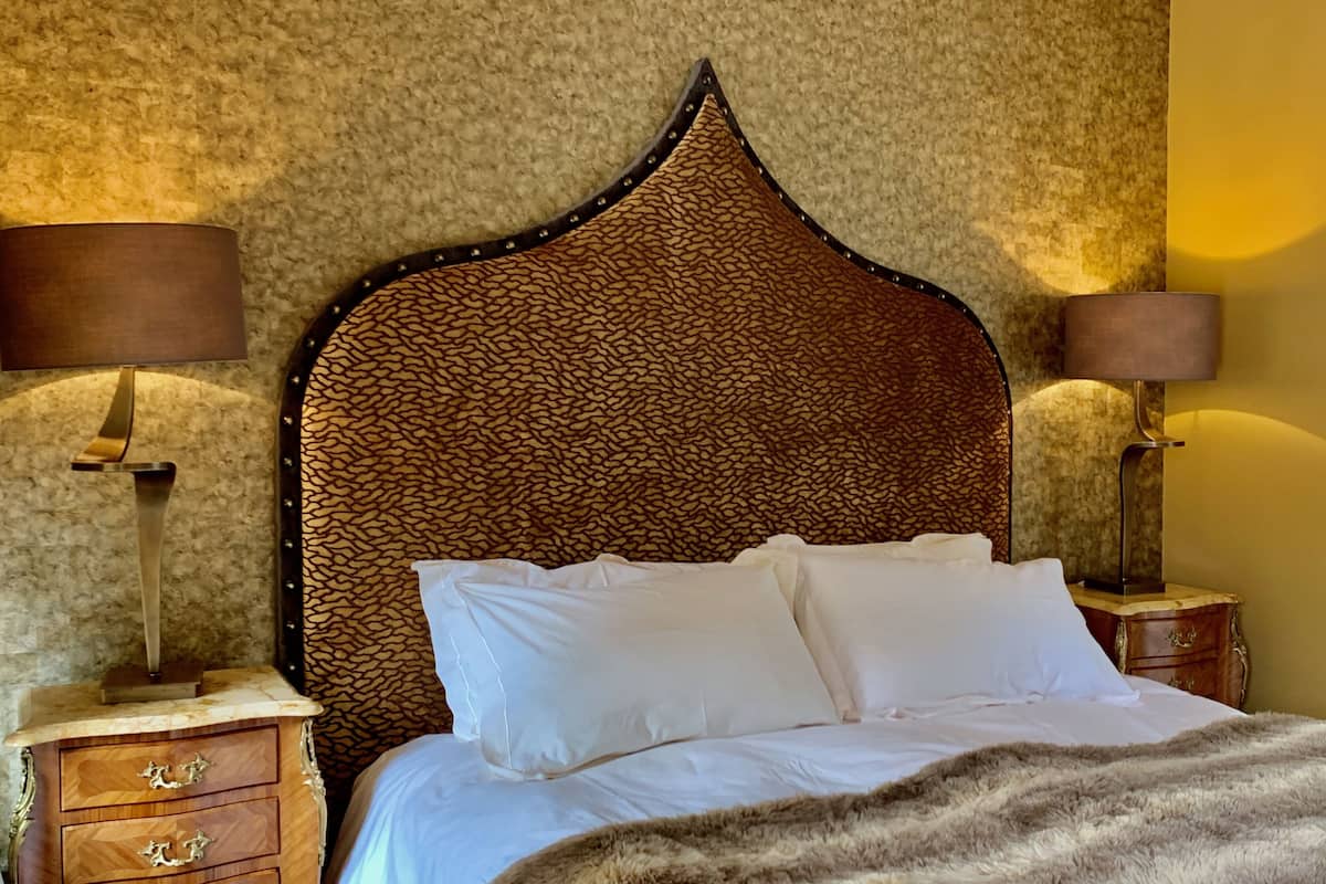 A neatly made bed with white linens, a headboard with a textured pattern, and two bedside lamps on wooden nightstands.