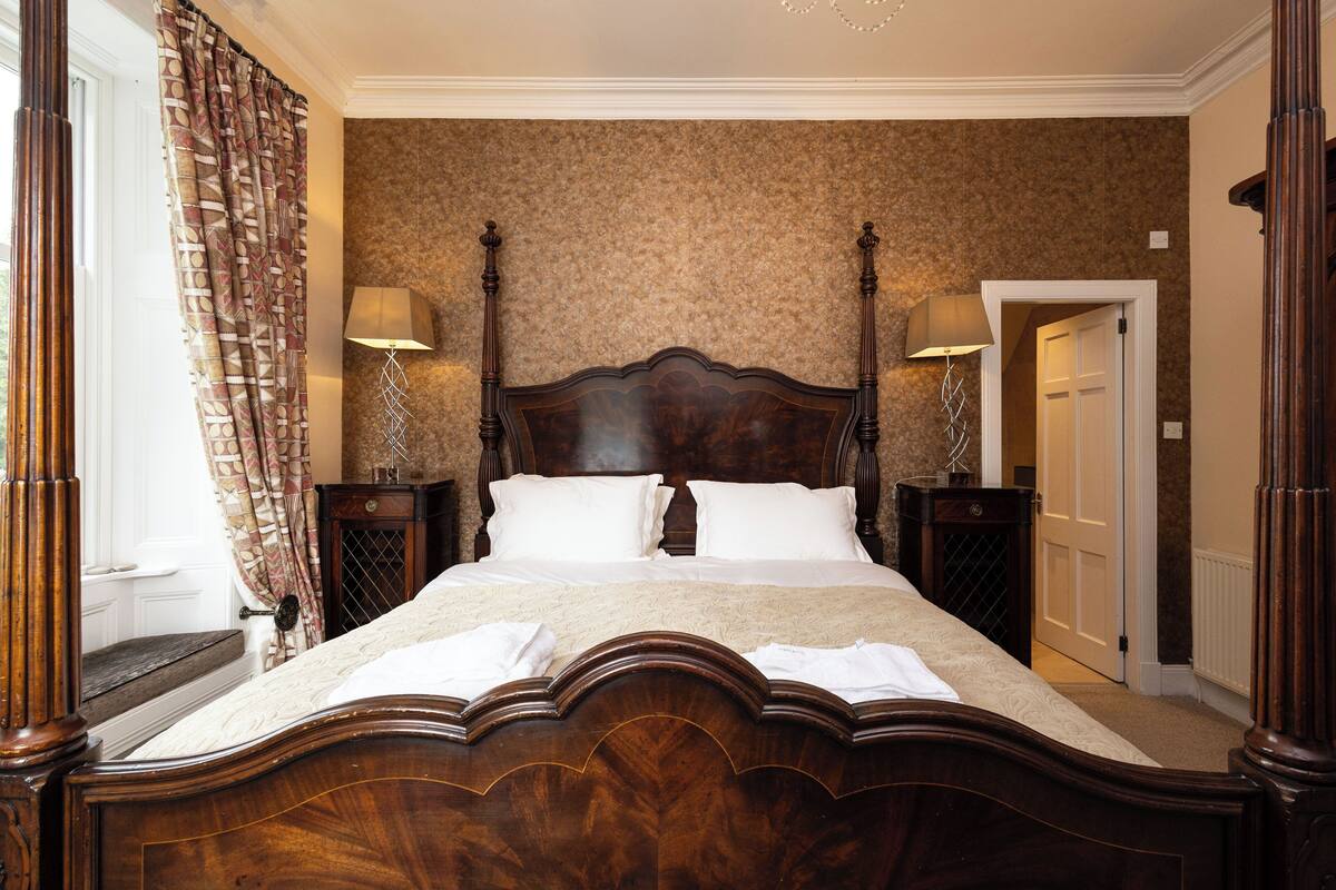 A large, ornate wooden bed with a headboard, two bedside tables with lamps, and a patterned wall behind.