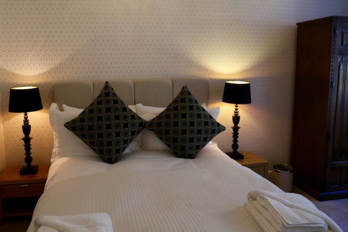 A neatly made bed with two decorative pillows, a bedside lamp, and a folded towel on the nightstand.