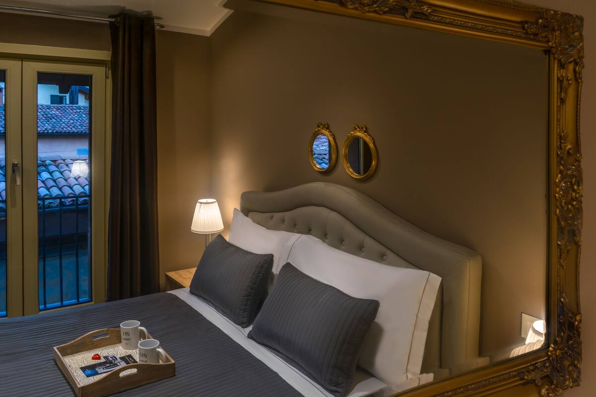 Une chambre d’hôtel avec un grand lit, deux tables de chevet, une commode, un plateau avec divers objets et une vue sur l’extérieur.