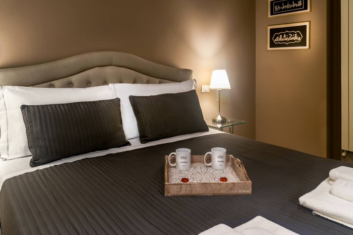 Une chambre d’hôtel avec un grand lit, deux oreillers, un plateau avec deux tasses et une lampe de chevet.