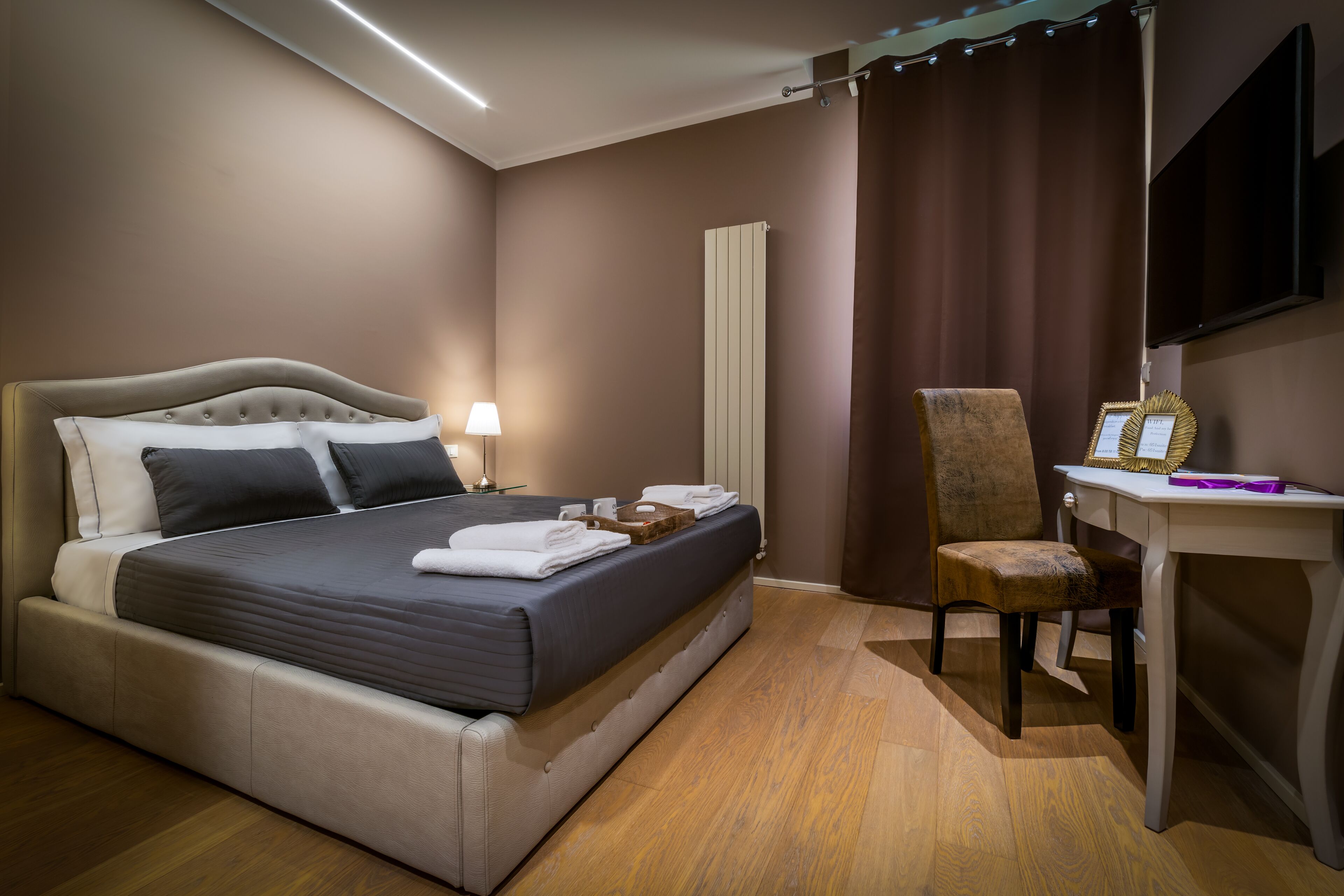 Quarto de hotel com uma cama grande, uma escrivaninha, uma cadeira e uma televisão de tela plana na parede.