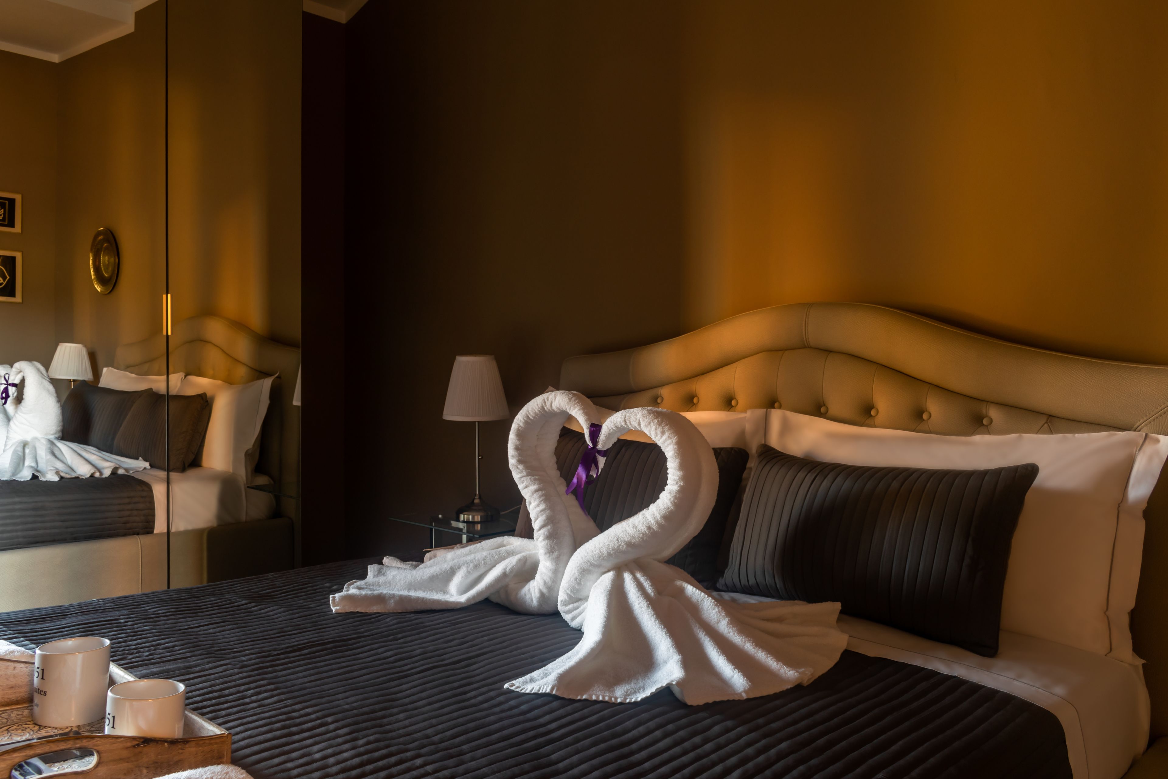 A hotel room with a bed, pillows, a bedside table with a lamp, and a mirror.