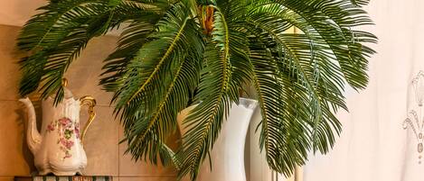 A bathroom with a potted palm plant, a white pitcher, a candle, a fresh water dispenser, and a framed sign.
