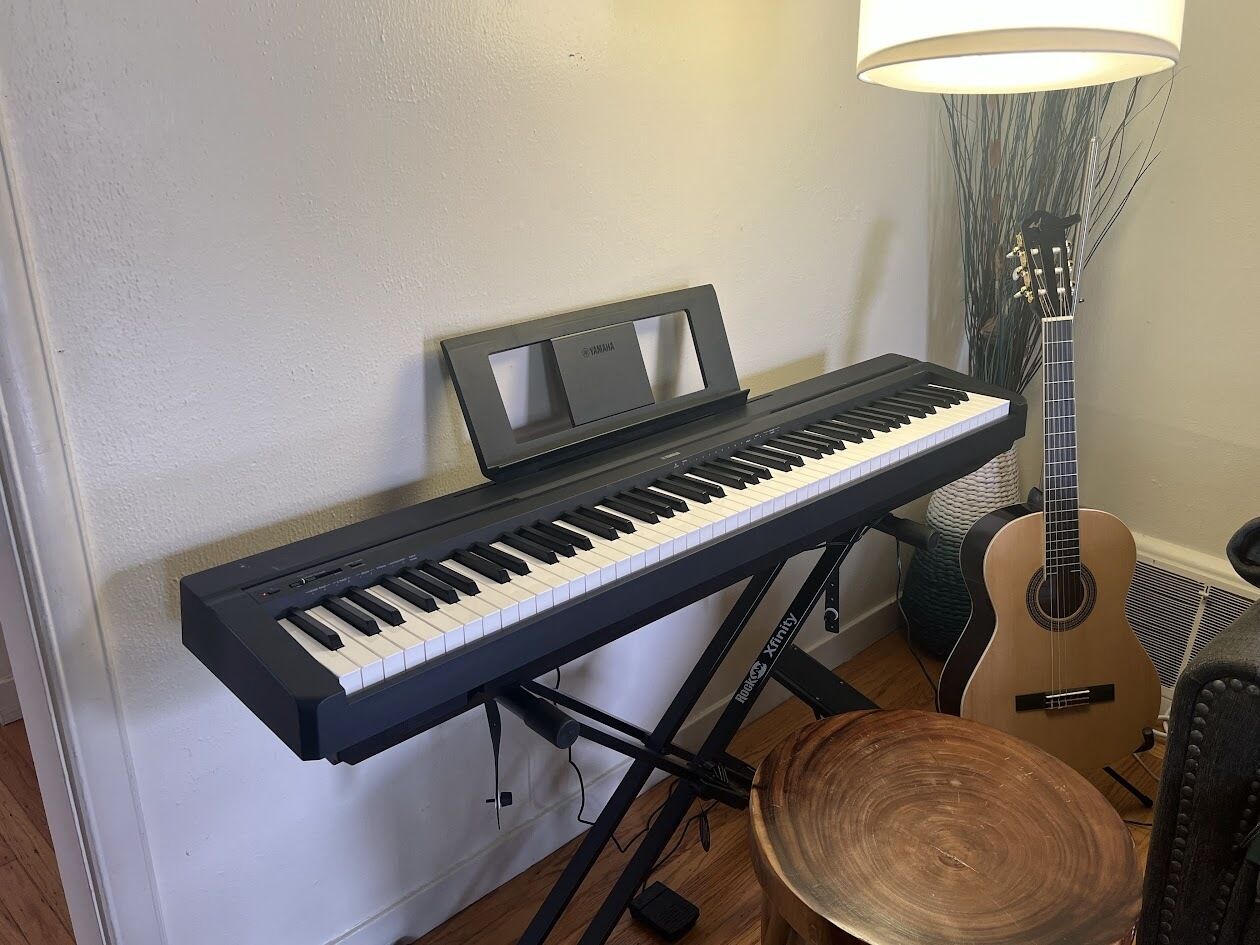 A keyboard on a stand, a guitar, and a lamp in a room.