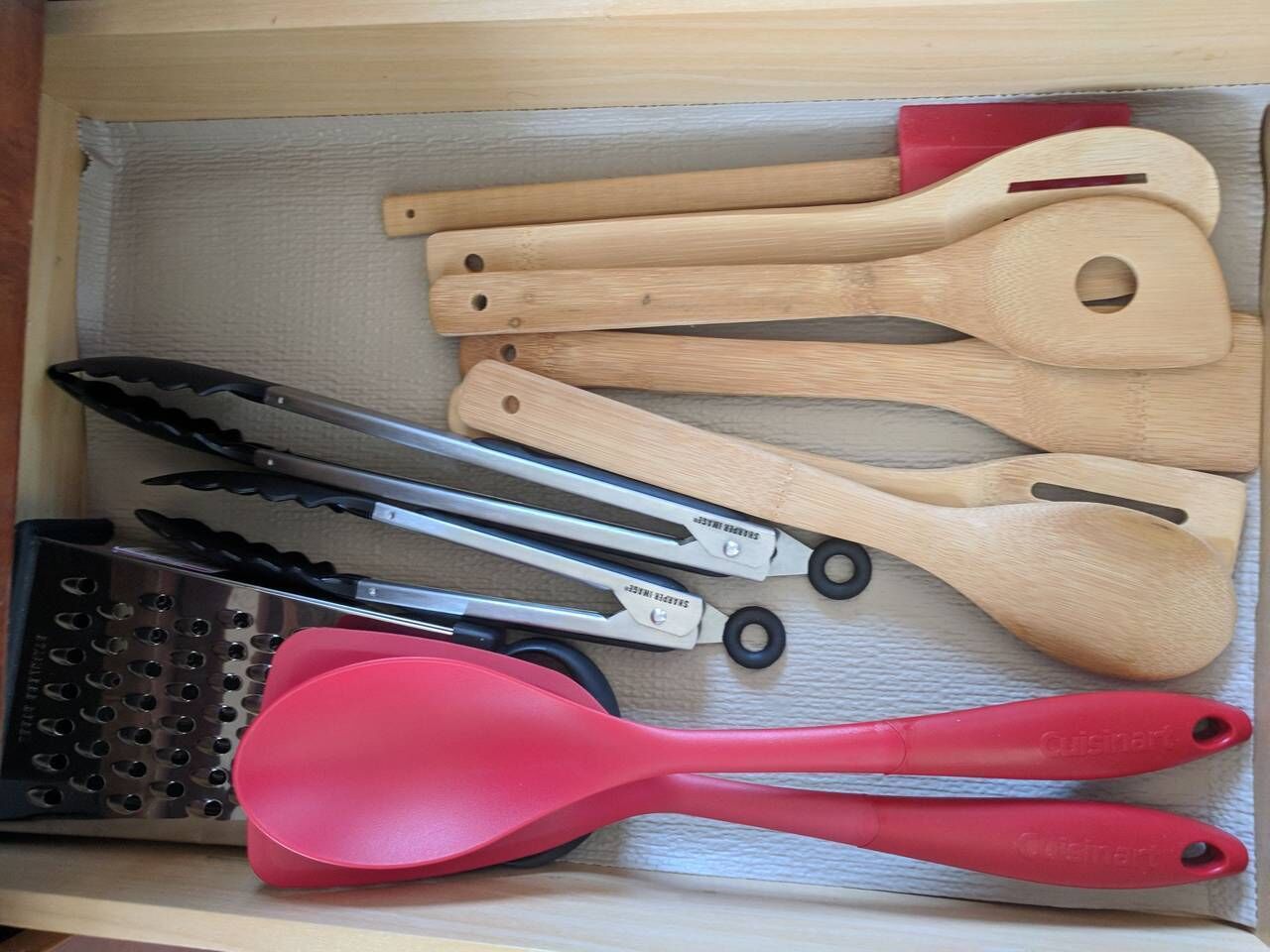 A drawer containing various kitchen utensils including a grater, tongs, and wooden spoons.